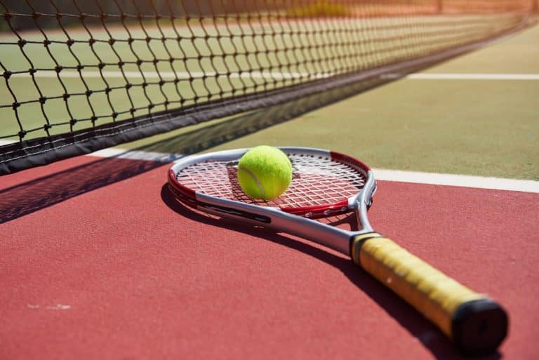 raquette de tennis avec balle de tennis dessus en gros plan posé sur le terrain a coté du filet