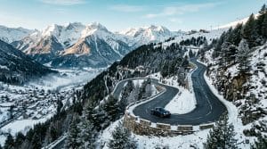 Voiture noire sur route de montagne sinueuse, paysage alpin enneigé