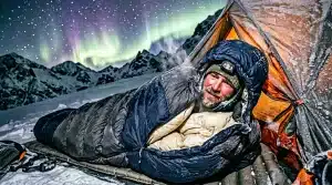 Campeur en sac de couchage sous aurore boréale montagne